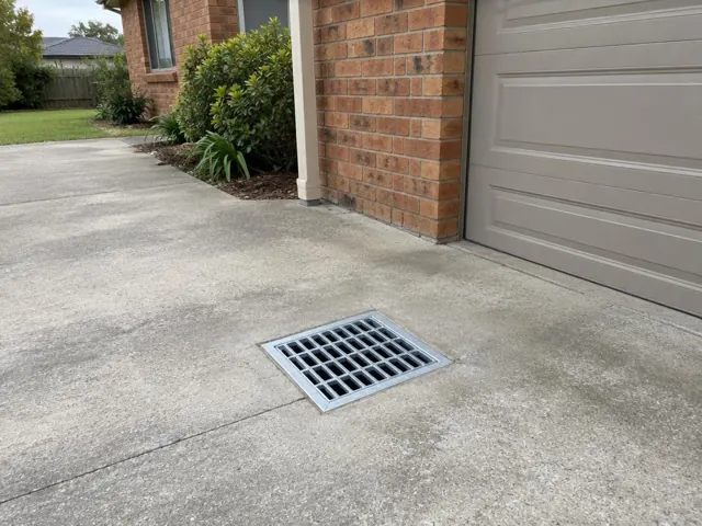 Concrete driveway with a metal outdoor drain grate beside a brick garage in Jewells