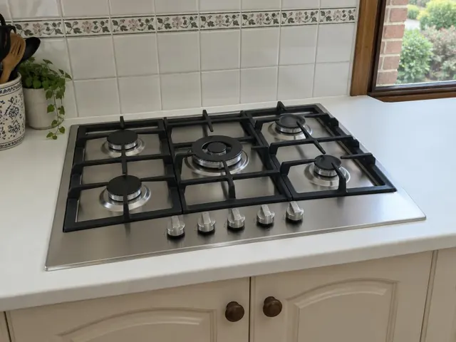 Stainless steel gas cooktop set into a white kitchen benchtop with tiled splashback in Dudley